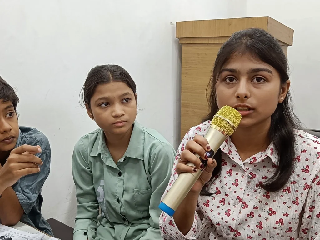 Students participating in an open discussion challenge with a microphone at AIM English Raipur